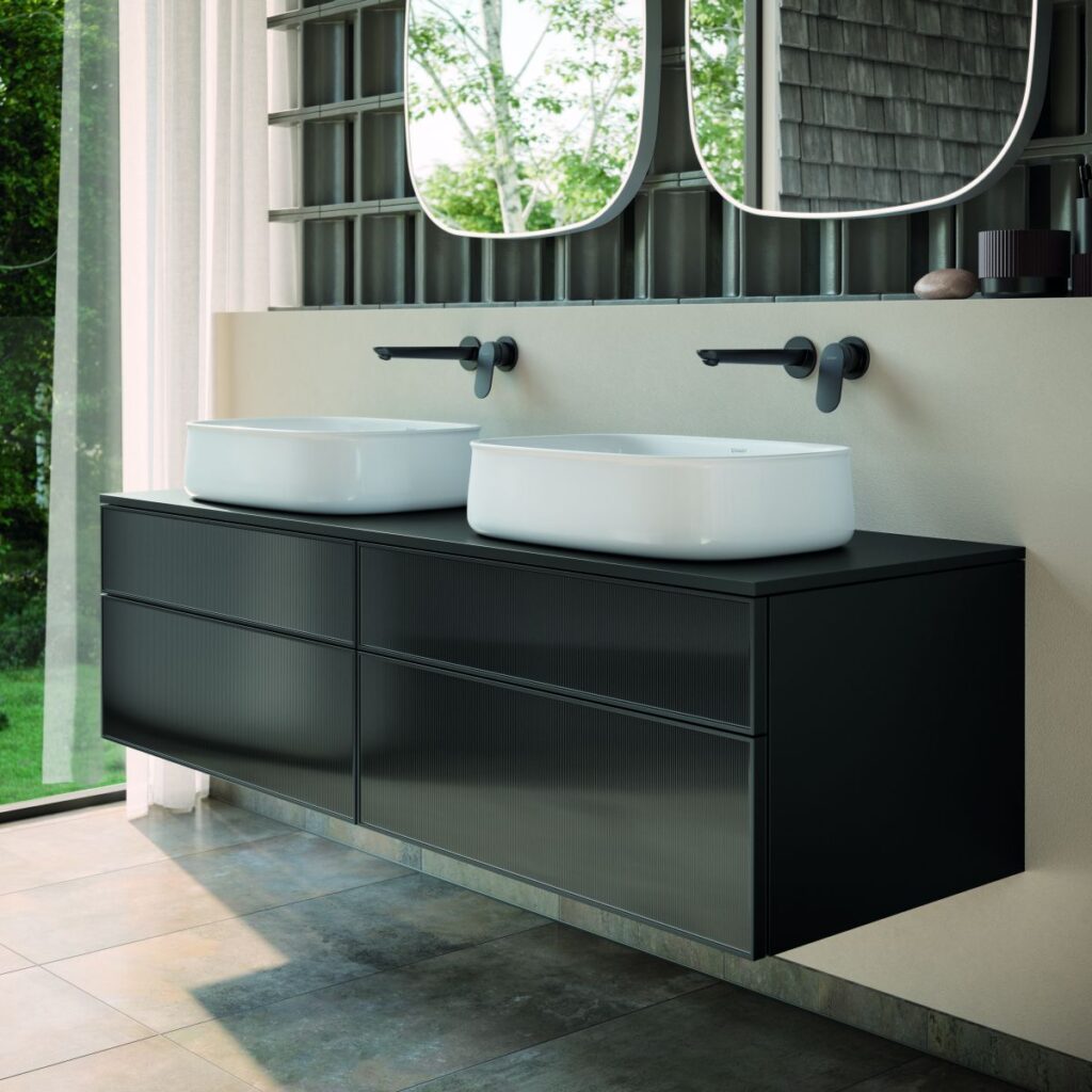 Linia spotyka krzywiznę: Minimalistyczne meble o wyrazistych krawędziach i dużej pojemności tworzą intrygujący kontrast z organicznymi formami ceramiki. Wersje z czarnego szkła strukturalnego nadają aranżacji wyjątkowo nowoczesny i elegancki charakter. Zencha to synonim lekkości i elastyczności – od otwartych półek po efektowną kompozycję z umywalką nablatową.
(Źródło zdjęcia: Duravit AG)