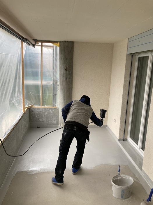 aplikacja systemu BFS, powierzchnia zagruntowana, detale uszczelnione w systemie Triflex ProDetail, + warstwa nośna Triflex ProFloor – na zdjęciu widoczny proces aplikacji Triflex Finish i aplikacja płatków Triflex Chips – aplikacja płatków odbywa się pneumatycznie przy użyciu pistoletu natryskowego, fot. Triflex 

